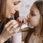 A mother and daughter sharing a strawberry milkshake indoors, depicting love and bonding.